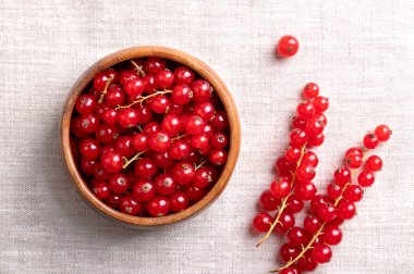 Kırmızı frenk üzümü, taze olgun ve ahşap bir kase içinde keten kumaş üzerinde işlenmemiş kırmızı frenk üzümü. Ribes Rubrum 'un küresel yenilebilir meyvelerini yemeye hazır. Kırmızı renkli tatlı meyveler. Yakın çekim yemek fotoğrafı..