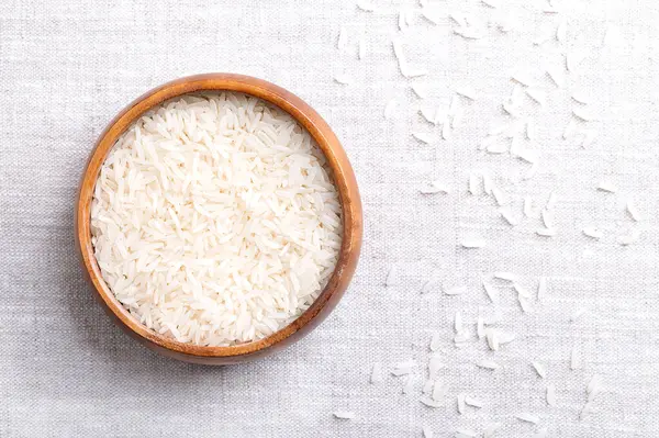 stock image White basmati rice, in a wooden bowl on linen fabric. Grains of long and slender grains with aromatic smell and taste. Rice grains of an Oryza sativa variety, cultivated in the Indian subcontinent.