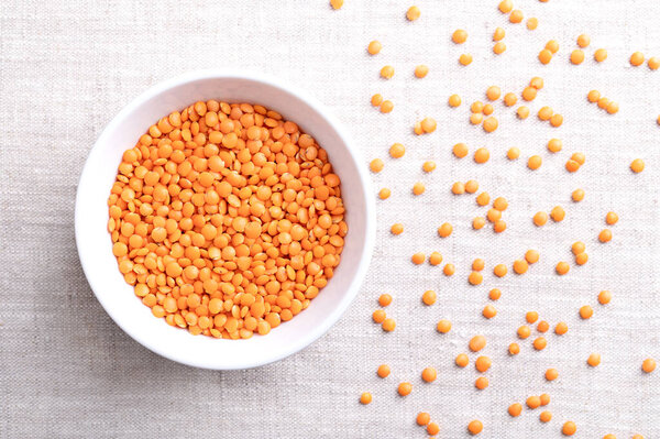 Красная чечевица в белой миске на льняном белье. Сорт чечевицы с шелухой удаляется для более короткого времени приготовления пищи и, чтобы избежать замачивания. Сушеные фрукты хрусталика culinaris, съедобный legume с семенами в форме линзы. Фото