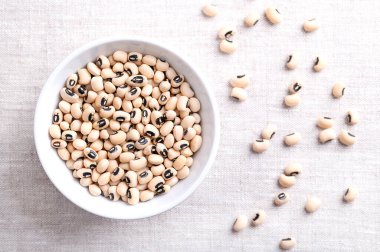 Dried black eyed peas in a white bowl over linen. Black eyed beans, or California blackeye, a legume of pale, medium-sized beans, with prominent black spot. Subspecies of cowpeas, Vigna unguiculata. clipart