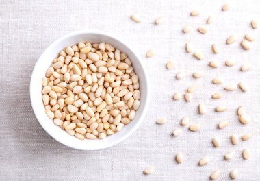 Keten kumaşın üzerinde beyaz bir kasede çam fıstığı. Pinoli, pinoli ya da pignoli olarak da bilinir. Kore çamlarının kabuklu tohumları ve meyveleri, Pinus Koraiensis. Pesto için kullanılır, tabağa eklenir ya da ekmeğe pişirilir..