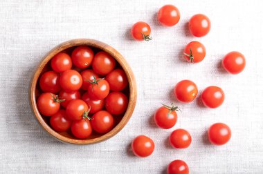 Small red cherry tomatoes in a wooden bowl on linen fabric, from above. Fresh, ripe, tiny and round cocktail tomatoes of the type Solanum lycopersicum var. cerasiforme, of juicy and sweet taste. clipart