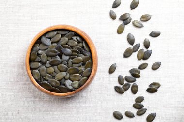 Ahşap bir kasede keten üzerinde Styrian yağı kabağı tohumları. Kurumuş, koyu yeşil ve taze meyveli balkabağı, Cucurbita peposu. Styriaca, tohum yağı için yetiştirilmiş sıradan bir balkabağı çeşidi..