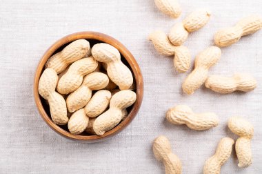 Ahşap bir kasede keten üzerinde kavrulmuş fıstık. Tam, çıtır fındık, Arachis hipogaea meyvesi doğal kabuğunda. Doğal, ceviz aromalı ve çıtır çıtır olan hafif altın atıştırmalık yiyecekler..