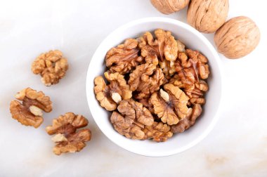 Ceviz çekirdeği yarım, beyaz bir kasede, mermer bir yüzeyde. Kabuklu ve kurumuş ceviz çekirdekleri, yaygın ceviz ağacı tohumları, Juglans regia, aperatif olarak ya da pişirmek için kullanılır. Yakından, yukarıdan..