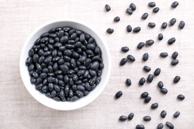 Siyah fasulye, beyaz kasede, keten üzerinde. Kurumuş fasulye çeşidi, Phaseolus vulgaris, ayrıca siyah kaplumbağa fasulyesi ve havyar krikolosu olarak da bilinir. Saten siyah tenli ve beyaz merkezli fasulye türü..