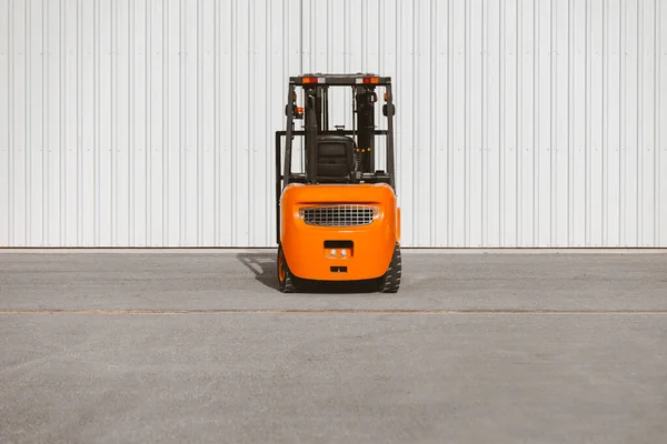 Forklift, reliable heavy loader parked next to the gates of hangar. Industrial vehicle.