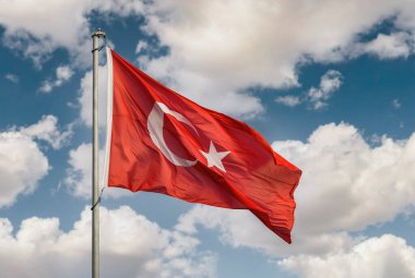 Güneşli bir günde bulutlu gökyüzünde dalgalanan Türkiye bayrağı. Mavi gökyüzünün önünde yıldız ve hilal ile güzel Türk bayrağı. Vatanseverlik ya da milliyetçilik.