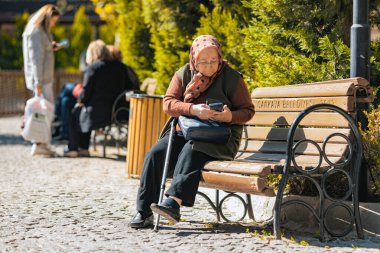 Ankara-Türkiye: 12 Ekim 2023: Ankara 'da güneşli bir günde parkta bankta otururken akıllı telefonunu kullanan yaşlı bir Türk kadın.