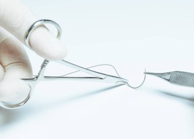 Cerrahlar yarım daire tutup beyaz arka planda penslerle iğne ve dikiş atıyorlar. Dikiş ipliği, tıbbi