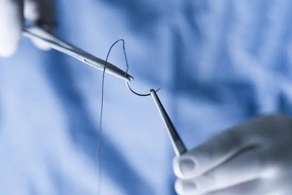 手術縫合を細心の注意を払って青いスクラブで手をクローズアップ 縫合を扱うスクラブの医療専門家 操作の間に力および針のホールダーが付いている半円針を握るオペレータ — ストック写真
