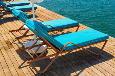Sıcak bir yaz gününde tahta bir iskelede turistleri bekleyen bir grup lüks güneş yatağı. Seyahat, turizm, tatil ve tatil kavramı.