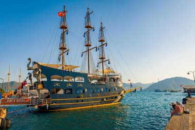Marmaris-Mugla-Türkiye: 24 Ağustos 2024: Marmaris Marina 'da insanlar gün batımından önce balık tutarken bir korsan tur botu iskeleye yanaştı. Korsan gemileri turistik yerlerde çok popüler turistik ilgi odağıdır.. 