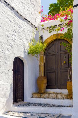 Eski ahşap kapılar, beyaz duvarlar, seramik kaplarda bitkiler ve antik Lindos, Rhodes 'ta basamakları olan güzel bir binanın girişi. Ada.