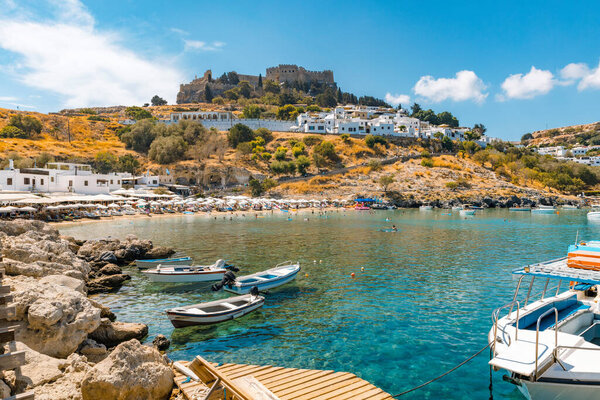 Вид на море, пляж и Акрополя в Линдосе. Туристы, идущие по дороге к городской площади. 
