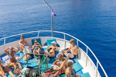 LINDOS-GREECE: 26 Ağustos 2024: Bir gezi teknesinin pruvasında güneşlenen bir grup tatilci. İnsanlar yazın denizde iyi vakit geçiriyorlar..