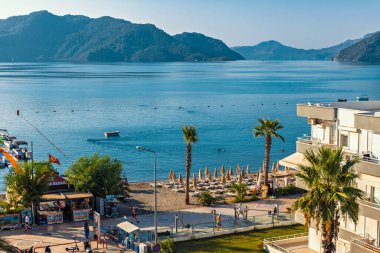 25 Ağustos 2024 'te Marmaris' te uzak dağlar ve açık mavi bir gökyüzü tarafından çerçevelenmiş teknelerle dolu canlı bir körfeze bakan bir otel..