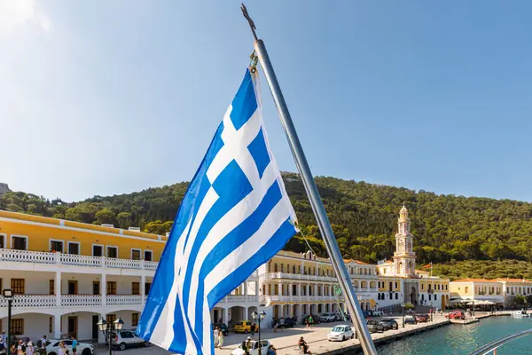 SyMI-GREECE: 27 Ağustos 2024: Yunan bayrağı ön planda belirgin bir şekilde dalgalanırken, başmelek Michael 'ın binaları ve arka planda görünen kule .