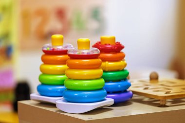 Parlak bir anaokulu ortamında oynamaya hazır ahşap bir yüzey üzerinde canlı, renkli bir yığın oyuncak duruyor. Bu resim çocukluk eğitimini ve eğlenceli keşifleri çağrıştırıyor..