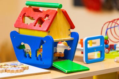 Canlı ahşap bir oyuncak ev, hayvan kesikleri ve bir şekil ayırıcı içeren, bir anaokulunda açık ahşap bir yüzey üzerinde oturur. Bu ilgi çekici aktivite oyuncağı küçük çocuklar için eğlenceli öğrenmeyi teşvik ediyor..