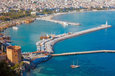 Bir hava manzarası, hareketli bir limanı, manzaralı bir kıyı şeridini ve Alanya 'daki tarihi kalesini ve deniz fenerini yakalar. Kasabanın canlı marinası bir dağ zeminine ve genişleyen bir şehre karşı teknelerle dolu..