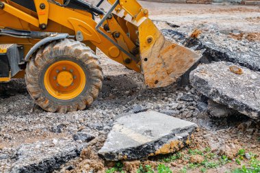 Büyük kovalı sarı bir inşaat aracının beton moloz ve kaldırımı parçaladığı görülüyor. Güçlü makine kentsel yıkım ya da yol onarım işiyle meşgul..