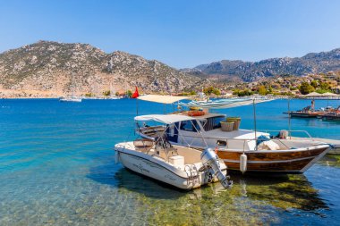 Selimiye-Marmaris: 30 Ağustos 2024: Birinde çizgili tepe örtüsü olan iki tekne, inanılmaz derecede temiz su bulunan bir körfeze demirlemiştir. Manzaralı arka planda yeşil tepeler ve parlak mavi bir gökyüzü var. Mükemmel bir yaz gününü yakalıyor..