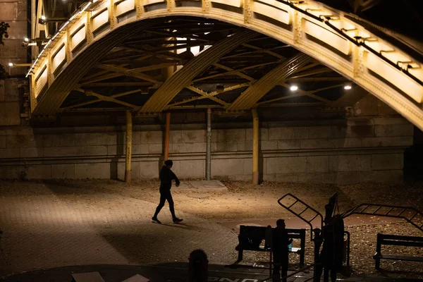 stock image Budapest, Hungary A man walks under the Margaret bridge at night and an outdoor exercise station.