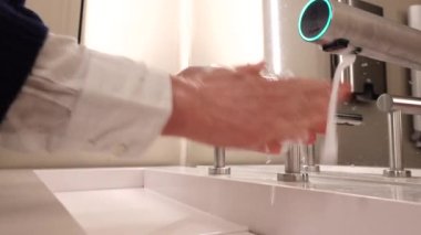 A woman washes her hands in a modern sink with a hot air faucet for drying.  