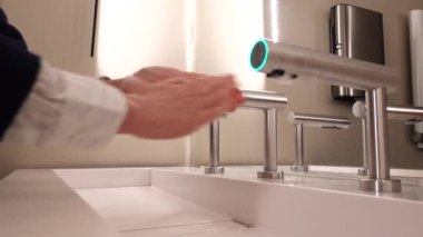 A woman washes her hands in a modern sink with a hot air faucet for drying.  