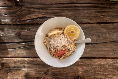 Copenhagen, Denmark  A bowl of granola and dried  pineapple fruit with a spoon on a wooden table.