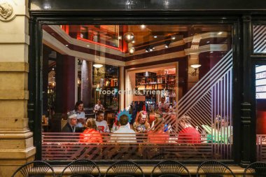 The Hague, Netherlands Friends eating dinner together in alarge restaurant seen through a window.