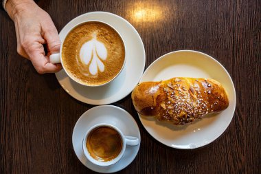 Malmo, Sweden Two coffees on a cafe table with a sweet bun and hands.