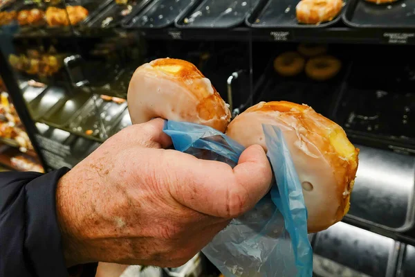 Glazed donuts and a hand in a supermarket.