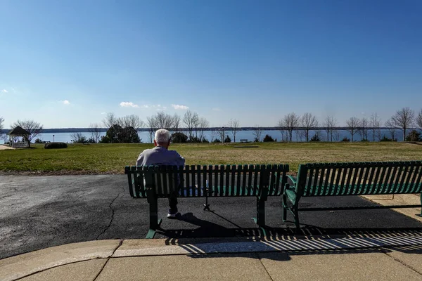 メリーランド州ソロモンズ昼間パトゥセント川を眺めながら屋外のベンチに座っている老人 — ストック写真
