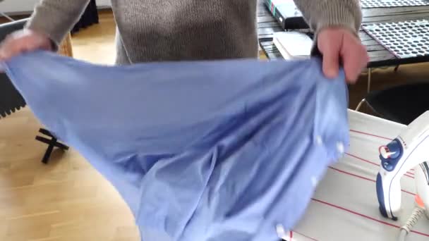 Ein Mann Bügelt Ein Blaues Hemd Auf Einem Bügelbrett — Stockvideo