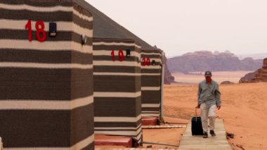 Wadi Rum, Jordan, bir adam çöl kampına gitmek için tahta yolda çantasıyla yürüyor..
