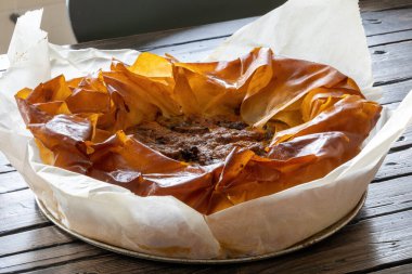 Tahta bir masada oturan kabak dolu çıtır bir tereyağlı börek..