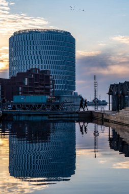 Kopenhag, Danimarka 'da küçük bir köprüde yürüyen insanlar Nordhavn bölgesindeki ahşap bir banyoda arka planda Amodern binası var..