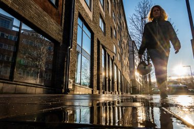 Stockholm, İsveç 'te yağmurdan sonra elinde motosiklet kaskı olan bir kadın güneşli ve ıslak bir sokakta yürüyor..