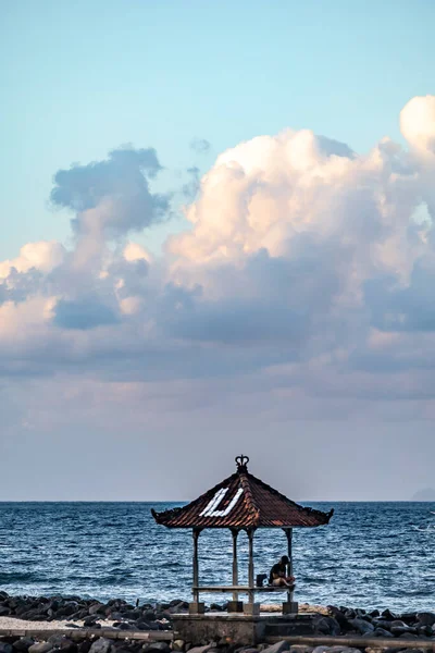 インドネシア バリのマンギスヘルメットを着た男がカンディダサ ビーチの海のそばの小さな塔に座っている — ストック写真