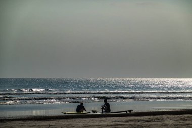 Seminyak, Bali, Endonezya Sörfçüleri gün batımında sahilde oturuyor..