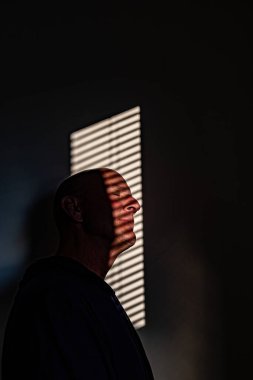 Orta yaşlı bir adamın portresi bir duvarda yansıtılan pencere perdelerine karşı.