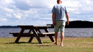 Mora, İsveç Bir adam yaz günü Siljan Gölü kıyısındaki bir parkta piknik masasına yürür. 
