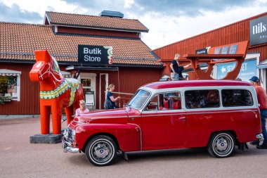 Nusnas, Sweden July 13, 2023 An old Volov car and people standing utside a retail store selling  traditional Dala Horses. clipart