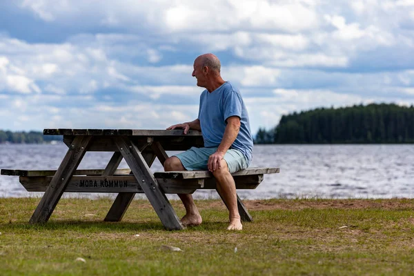 stock image Mora, Sweden A man sits at a picnic table on the shore of Lake Siljan.Sign says Mora Municipality in Swedish,