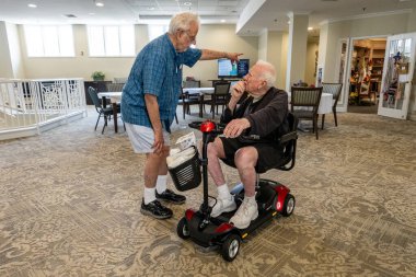 Solomons, Maryland, 27 Temmuz 2023. Huzurevinde elektrikli scooter kullanan yaşlı bir adam koridorda ayakta duran başka bir asistanla konuşuyor..