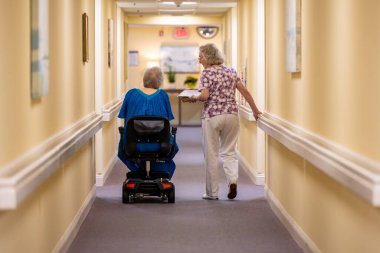 Solomons, Maryland ABD 3 Ağustos 2023 Biri sandalyedeki iki kadın lüks bir huzurevinde koridorda yürüyorlar..