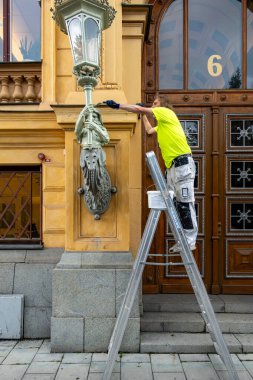 Stockholm, İsveç 15 Ağustos 2023 'te bir ressam klasik bir lamba ve heykeli SEB banka binasının ön cephesine boyamak için şehir merkezinde bir merdivenin üzerinde duruyor..