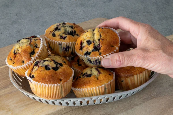 A hand reaches for fresh home baked blueberry muffins in a cafe basket.